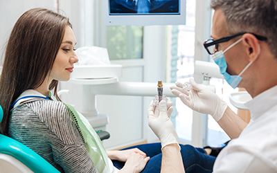 A male dentist showing a dental implant to his patient